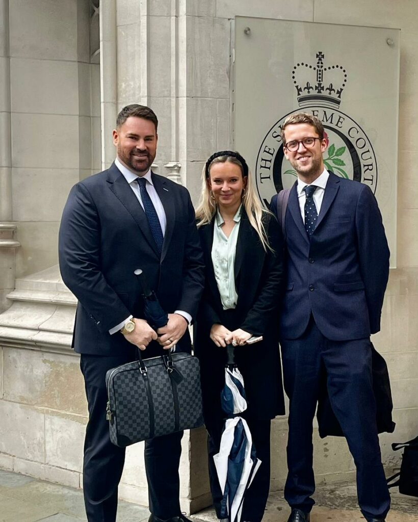From left: Byron James, Antonia Church and Jack Mitchell are wearing dark suits, standing outside the entrance to the Supreme Court building.