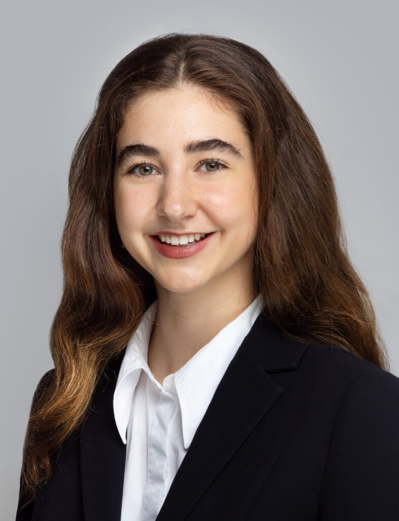 Melissa has long, wavy dark brown hair. She's smiling at the camera. She wears a white collared shirt and black jacket.