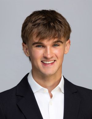 Jack has short brown hair, wears a white shirt and black blazer, smiling at the camera.